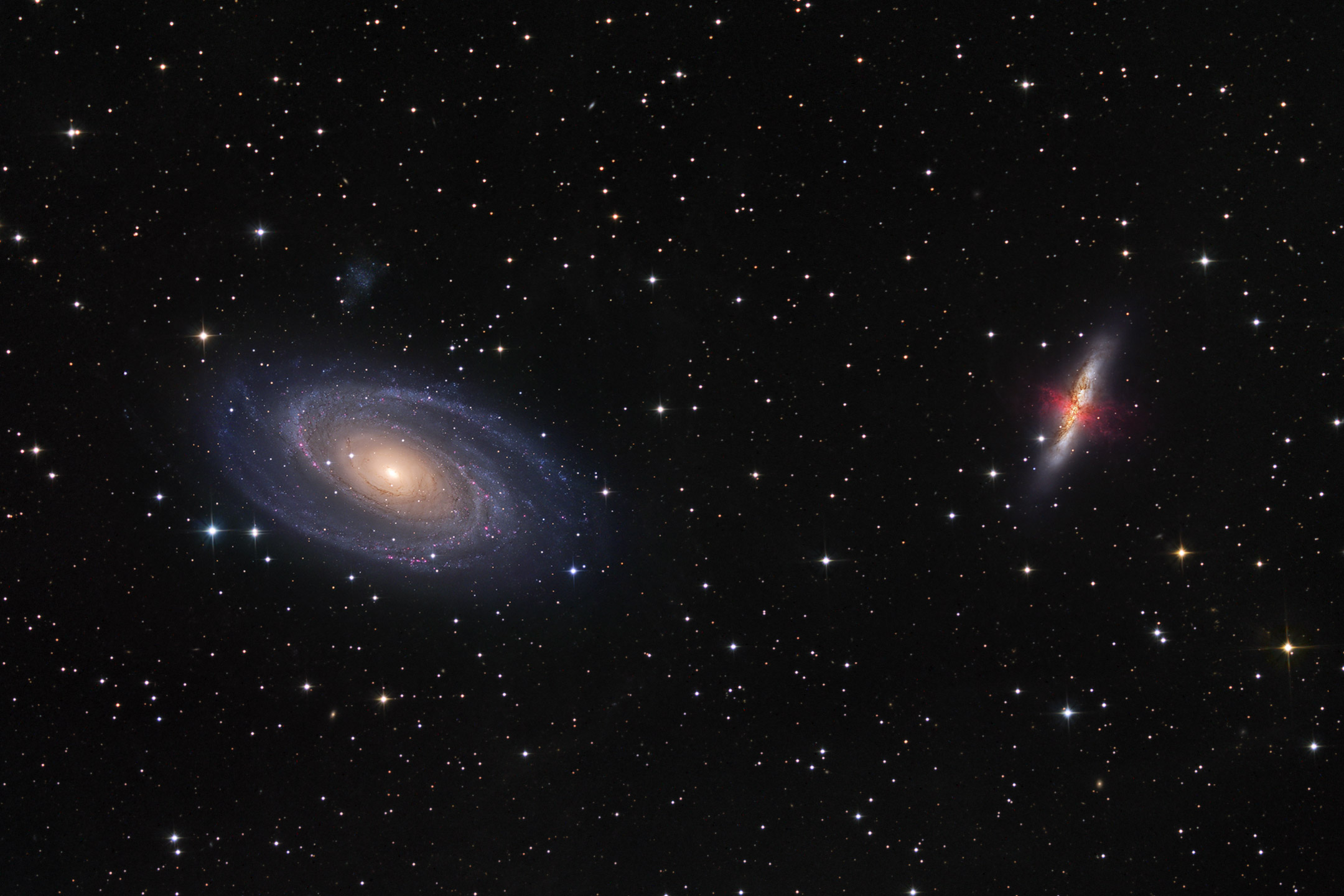 Galaxy M81 is on the left surrounded by blue spiral arms. On the right marked by massive gas and dust clouds, is Galaxy M82.