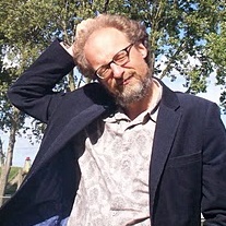 Man with glasses in blue jacket scratching head, photo in the open air