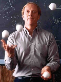 Ron juggling with four balls in front of blackboard