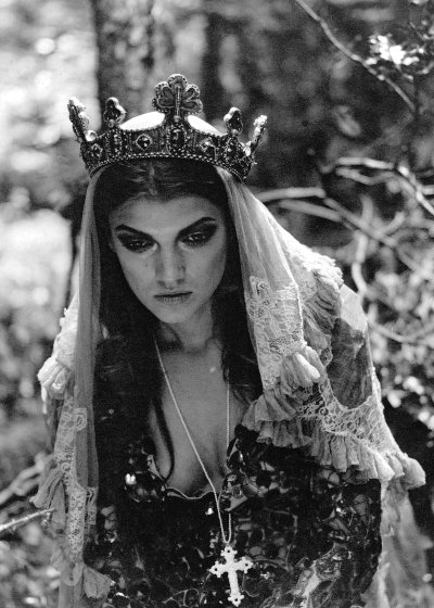 Gothic queen with crown and crucifix bends over in forest
